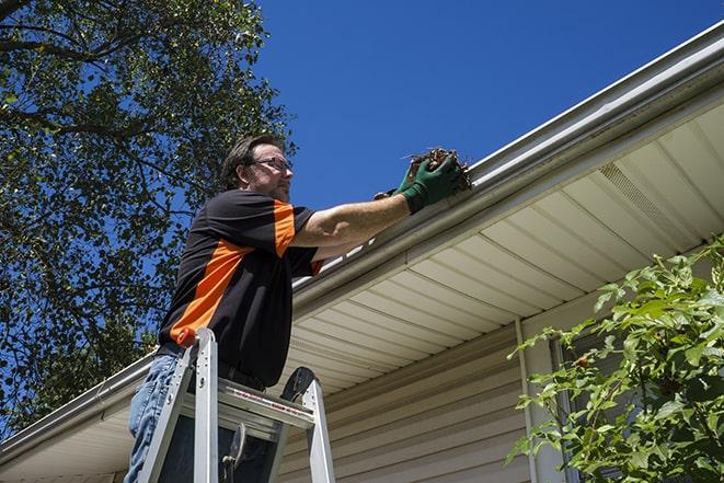 man using a ladder to fix a broken gutter in Babson Park MA